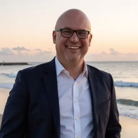 Man on the beach in a collared shirt and dark blazer smiling